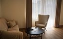 Een gezellige woonkamer met een lichte bank en een comfortabele fauteuil. Het licht stroomt door de gordijnen en creëert een uitnodigende sfeer.