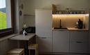 Een moderne keuken met minimalistische meubels en een kleine tafel. Het licht verlicht het aanrecht en creëert een uitnodigende sfeer.