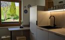 Een moderne keuken met een heldere werkblad en een zwarte gootsteen. Door het raam zijn groene bomen en een zonnig landschap te zien.
