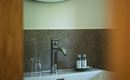 Een elegant badkamer met een wit wastafel en een moderne kraan. Een ronde spiegel en een glas water completeren de stijlvolle ambiance.