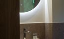 Een modern badkamer met een elegant wastafel en een ronde spiegel. Op de plank staan twee flesjes.