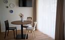 Een gezellige eetruimte met een ronde tafel en drie stoelen. Aan de muur hangen decoratieve borden, en grote ramen laten veel licht binnen.