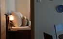 Een gezellige kamer met een bed, dat is uitgerust met grote kussens. Op de achtergrond staat een lamp en decoratieve borden aan de muur.