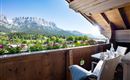 Ein schöner Balkon mit Blick auf die Berge und eine grüne Landschaft. Sonnenschein und Blumen verleihen der Szene eine einladende Atmosphäre.