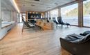 A modern wellness area with wooden floors and large windows that offer a view of snow-covered mountains. There are comfortable loungers and an open reception area.