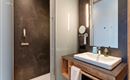 A modern bathroom with a shower and an elegant sink arrangement. The walls are in dark shades, complemented by bright lighting.