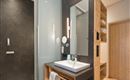 A modern bathroom with a glass shower and a stylish sink unit. The walls are done in dark and warm wood tones.