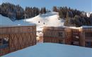 A modern wooden building in the mountains, surrounded by snow-covered hills. In the background, ski lifts and a snowy slope are visible.