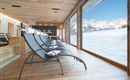 A modern relaxation room with loungers and large windows that offer a stunning view of snow-covered mountains. The bright wood and cozy atmosphere invite relaxation.
