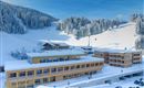 A modern hotel in a snowy landscape. In the background, there are snow-covered mountains and skiing activities visible.