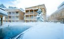 A modern hotel in a snowy landscape. The exterior features a pool, surrounded by snow and wooden architecture.