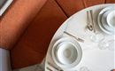 Ein eleganter Esstisch mit weißen Tellern, Besteck und Gläsern. Die orangefarbene Sitzbank bietet eine gemütliche Atmosphäre.