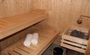 Eine gemütliche Sauna aus Holz mit zwei Bänken und sauberen Handtüchern. Neben der Saunabank befinden sich ein Saunaofen und ein Eimer.