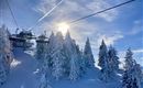 A picturesque winter landscape with snow-covered trees and a ski lift. The sun shines over the snow-rich hills.