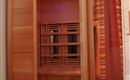 A sauna with wooden paneling and colorful lights. It is located in a room with a curtain and a mirror.