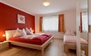 A cozy bedroom with red walls and a large bed. The room has large windows and a modern wardrobe.