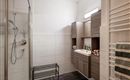 A modern bathroom with a shower and wooden cabinets. The walls are brightly tiled and a towel rack is located on the wall.