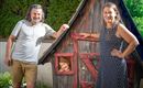 A happy couple stands next to a small wooden house. A child looks cheerfully out of the window of the house.