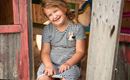 A happy girl is sitting in a small playhouse. She is wearing a striped dress and is smiling.