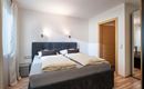 A cozy bedroom with a double bed and soft bedding. There are light walls and a large mirror that additionally brightens the room.