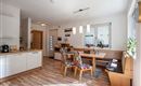 A modern kitchen with a dining table and colorful chairs. Plenty of light flows through the windows, and the wood design creates an inviting atmosphere.