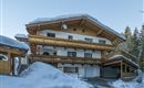 A charming building in alpine style, surrounded by snow. The wooden balconies and the design give the house a cozy atmosphere.