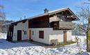 Ein traditionelles Haus im Alpenstil, umgeben von Schnee. Der klare blaue Himmel sorgt für eine ruhige Winteratmosphäre.
