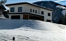 A modern house in a snowy landscape. In the background, mountains and blue sky can be seen.