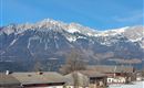 Eine majestätische Berglandschaft mit schneebedeckten Gipfeln und klarem blauem Himmel. In der Vordergrund sind traditionelle, alpine Häuser zu sehen.