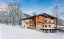 A beautiful building in the snow with a traditional wood design. The surroundings are surrounded by wintry mountains and trees.