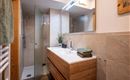 Een moderne badkamer met een douche en een houten wastafel. De wanddecoratie is in neutrale kleuren en er zijn verse planten als decoratie.
