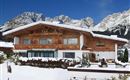 A beautiful chalet in the snow, surrounded by majestic mountains. The clear blue sky gives the winter landscape a serene atmosphere.