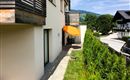 Eine moderne Terrasse mit einem Sonnenschirm und Blick auf die Hecke. Im Hintergrund sind sanfte Hügel und Bäume zu sehen.