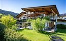 A modern house with a spacious garden and terrace. The surroundings are green and surrounded by mountains.