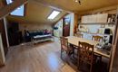 A bright attic apartment with a living room and a small kitchenette. The dining area is equipped with a wooden table and chairs.