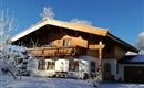 A beautiful wooden house in Alpine style, surrounded by snow-covered trees. The clear blue sky gives the scene a peaceful atmosphere.