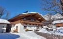 A traditional chalet in winter with a snow-covered plot. The blue sky and the surrounding trees give the scene a serene atmosphere.