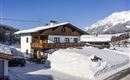A charming house in the snow with a balcony and a beautiful mountain landscape in the background. The surroundings are wintry and peaceful.
