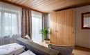 A cozy bedroom with a wooden ceiling and bright curtains. The room is decorated with a large wardrobe and a plant.