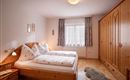 A cozy bedroom with two single beds and wooden furniture. The room is bright and friendly, with a window that lets in plenty of light.