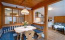 A cozy kitchen with a wooden style and a dining table. The decor is bright and friendly, with blue fabric covers and a beautiful bouquet of flowers on the table.