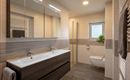 A modern bathroom with two sinks and large mirrors. It features bright tiles and a shower with glass partition.