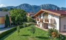 A beautiful house with a balcony and flower boxes. In the background, impressive mountains and a green meadow can be seen.