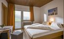 A modern bedroom with a double bed and a cozy wooden ceiling. Large windows let in plenty of light and offer a view of the greenery.