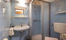 A small bathroom with blue tiles. It contains a shower cabin, a sink, and a toilet.
