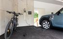 A modern garage environment with an e-bike and an electric car, both of which are charging. On the wall, there is a charging station for electric vehicles.