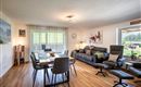 A modern living room with a large dining table and comfortable seating.  
Large windows let in plenty of light and offer a view of the outdoors.