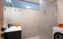 A modern laundry room with a shower and a washing machine. The walls are brightly tiled, and there are orange towels on the countertop.