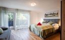 A modern bedroom with a double bed and a cozy sofa. Large windows provide plenty of daylight and a view of the greenery.