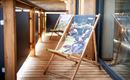 A cozy terrace with wooden lounge chairs. The chairs are decorated with colorful motifs and invite you to relax.